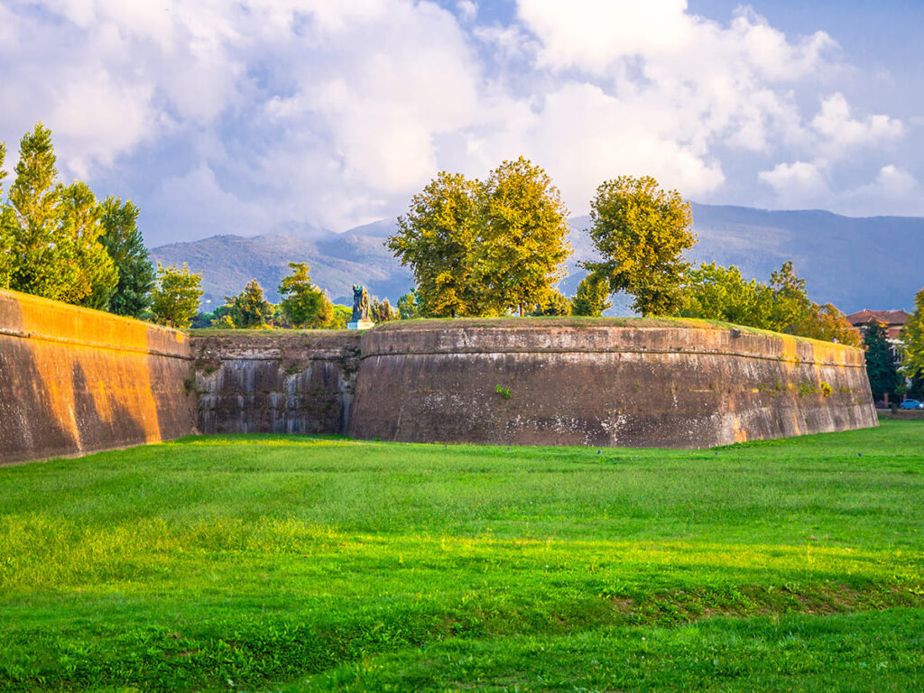 ITS__0007_Defensive brick city wall, grass green lawn, trees and Tuscany hills and mountains with beautiful cloudy eveni